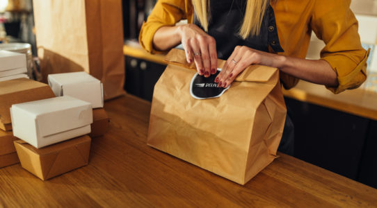 Close up of a hospitality worker packing food in paper bags and preparing them for delivery